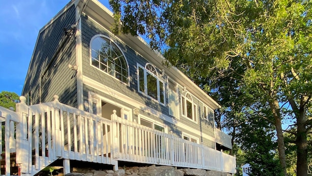 A two-story house with a white picket fence, a stone foundation, and a garden with red flowers. - Sunny Beach Getaway-Outdoor Shower, Big Deck, Walk to Coffee+Ice Cream-Sleeps 10 (Narragansett)