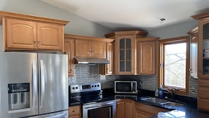 A modern kitchen with stainless steel appliances, wooden cabinets, and a large window. - Sunny Beach Getaway-Outdoor Shower, Big Deck, Walk to Coffee+Ice Cream-Sleeps 10 (Narragansett)