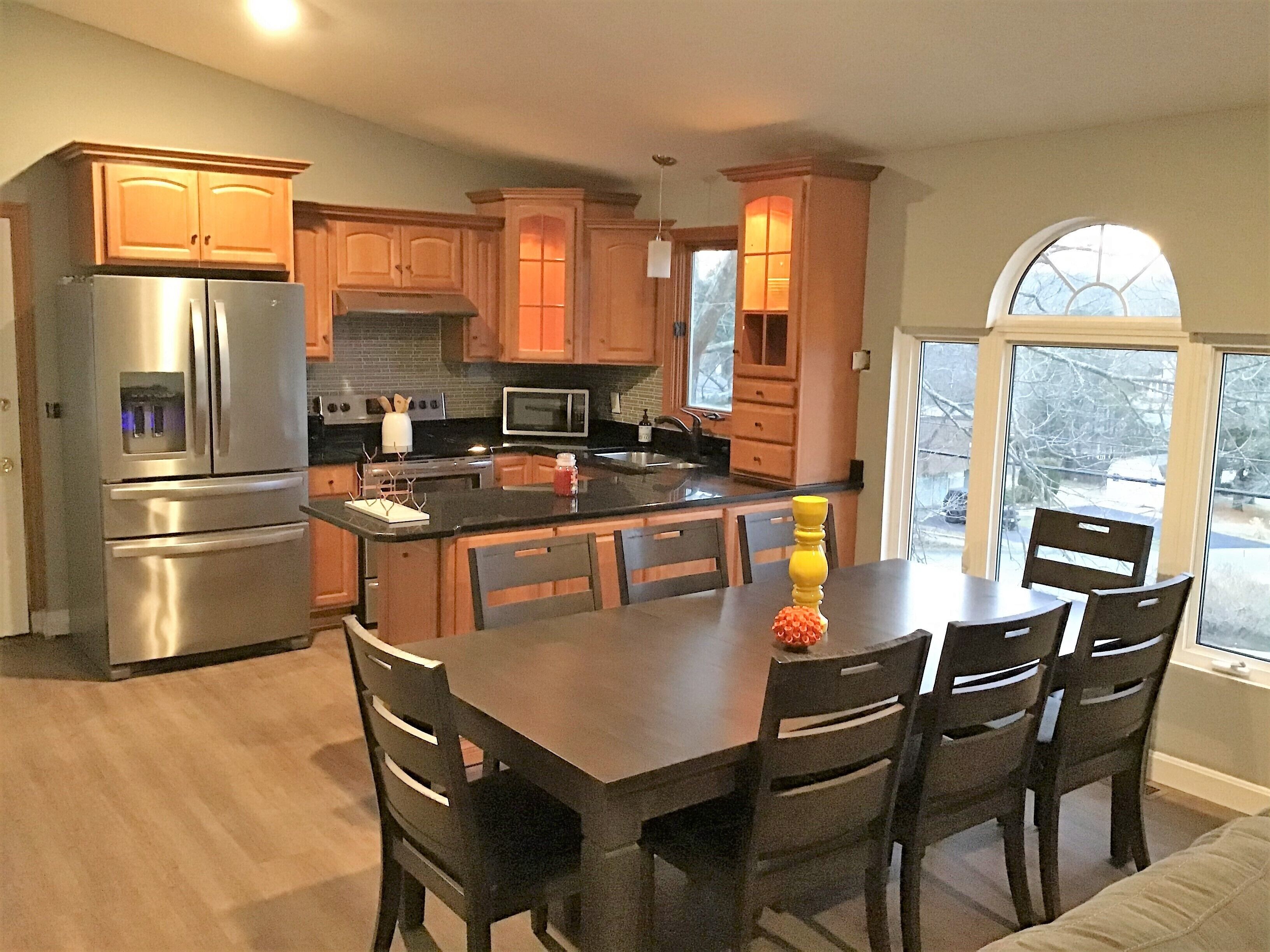 A modern kitchen with stainless steel appliances, wooden cabinets, and a central island with chairs.