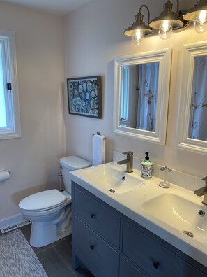 Une salle de bain avec des toilettes blanches, un lavabo surmonté d’un miroir et un tableau abstrait encadré accroché au mur.