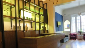 Un'area reception con scrivania in legno, mensole con bicchieri e un'area salotto con divano e poltrone viola.