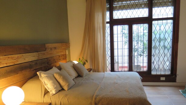 Camera da letto con testiera in legno, un letto con molti cuscini, una lampada da comodino e una finestra vista verde.
