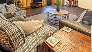 A cozy living room with a stone fireplace, plaid sofas, a round coffee table, and a television. - The Lower Deck on Riverview ~ direct river access (Mountain View)