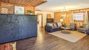 A modern living room with dark wood flooring, a black entertainment unit, and a seating area with a sofa and two armchairs. - The Lower Deck on Riverview ~ direct river access (Mountain View)