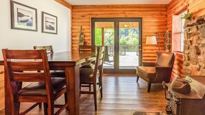 A wooden cabin interior with a dining table, chairs, a sofa, and a fireplace. - The Lower Deck on Riverview ~ direct river access (Mountain View)
