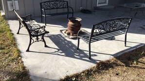 Un patio al aire libre con dos bancos de metal, una jardinera grande y una mesita.