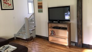 Una sala de estar con una escalera, un televisor sobre un mueble de madera y una estantería.