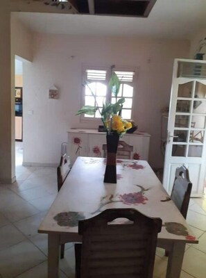 A dining area with a table, chairs, a vase with flowers, a window, and a white cabinet. - The jewels of tiv villa villa 5min from the beach with whirlpool bath (Fort-de-France)