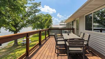 A wooden deck with a table and chairs, overlooking a body of water and trees.