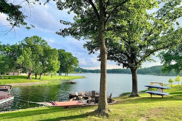 Un parque junto al lago con mesas de picnic, un muelle y barcos, y una zona cubierta de césped.