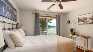 Una camera da letto con un letto grande, un ventilatore a soffitto, vista su un lago, un quadro e un tavolino consolle con una pianta.