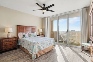 A hotel room with a bed, two nightstands, a ceiling fan, a large sliding glass door to a balcony, and a wooden dresser.