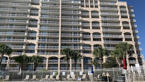 A multi-story hotel with a swimming pool, balconies, and palm trees.