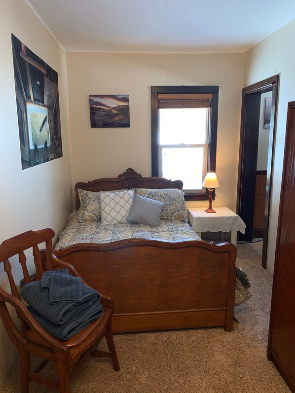 A bedroom with a wooden bed, a chair with folded clothes, a nightstand with a lamp, and two wall-mounted paintings. - Wild Grape Cottage - 8 Miles from Two Harbors and Lake Superior (Two Harbors)