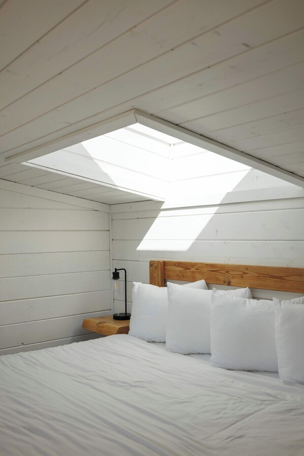 A bedroom with a skylight, wooden headboard, and white bedding.