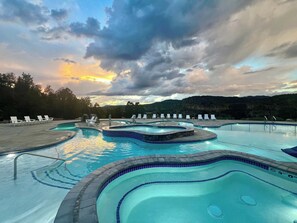 A multi-level swimming pool with lounge chairs and a mountainous backdrop.
