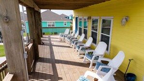 Een overdekt terras met witte lounge fauteuils en een gele muur.