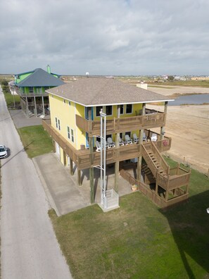 A multi-story building with a balcony and a deck, situated near a beach and a road.
