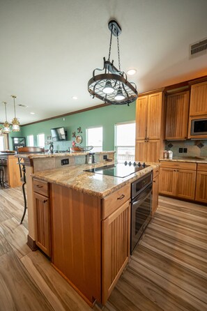 A kitchen with wooden cabinets, a granite countertop, stainless steel appliances, and a hanging light fixture.