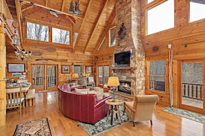 A log cabin interior with a stone fireplace, wooden ceiling, and large windows. - Pinch Me - Mr Lake Lure Vacation Rentals (Lake Lure)