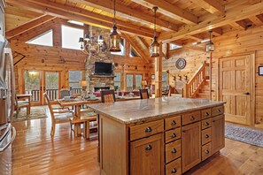Interior espacioso de una cabaña de madera con una isla grande en la cocina, comedor y una chimenea de piedra.