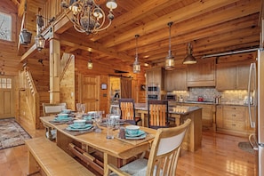 A wooden cabin interior with a dining area, kitchen, and staircase. - Pinch Me - Mr Lake Lure Vacation Rentals (Lake Lure)