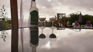 A bottle of Charrette on a reflective surface with two glasses, a bamboo plant, and outdoor furniture. - La Kazanou (Saint-Joseph)