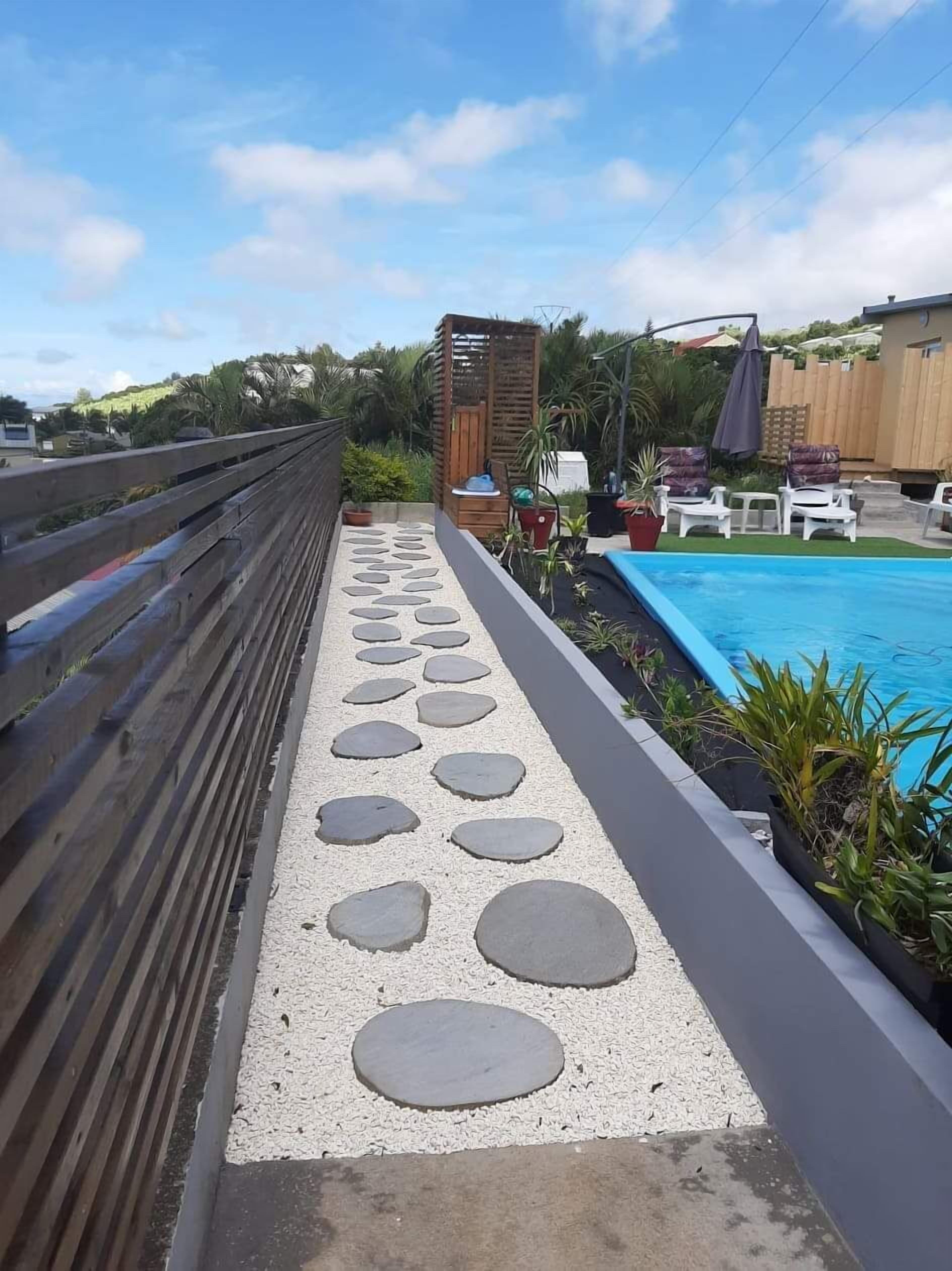 Un sentiero con pietre circolari conduce a una zona piscina con lettini e un pergolato in legno.