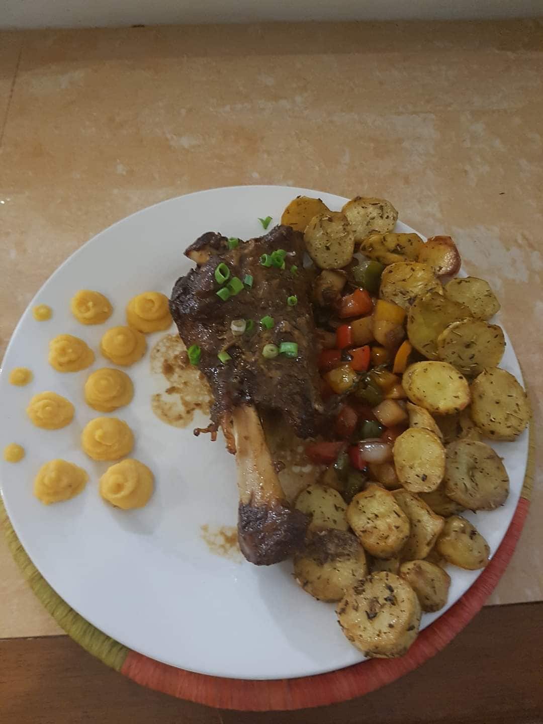 A plate with a roasted meat dish, roasted potatoes, and a side of yellow sauce.