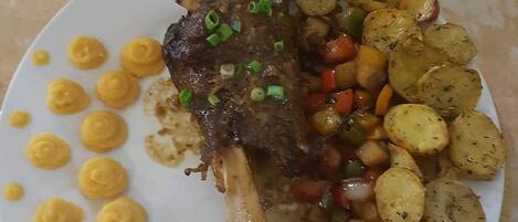 A plate with a roasted meat dish, roasted potatoes, and a side of yellow sauce.