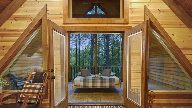 Ein gemütliches Holzhaus mit Schlafzimmer auf dem Dachboden, ausgestattet mit einem karierten Bett, einem Schaukelstuhl und Blick auf den Wald.