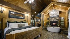 Ein Schlafzimmer aus Holz mit einem großen Bett, einem Kamin aus Stein und einer Badewanne.