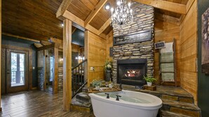 Ein Holzinnenraum mit Kamin aus Stein, einer Badewanne und einer Kristallleuchtre.'
