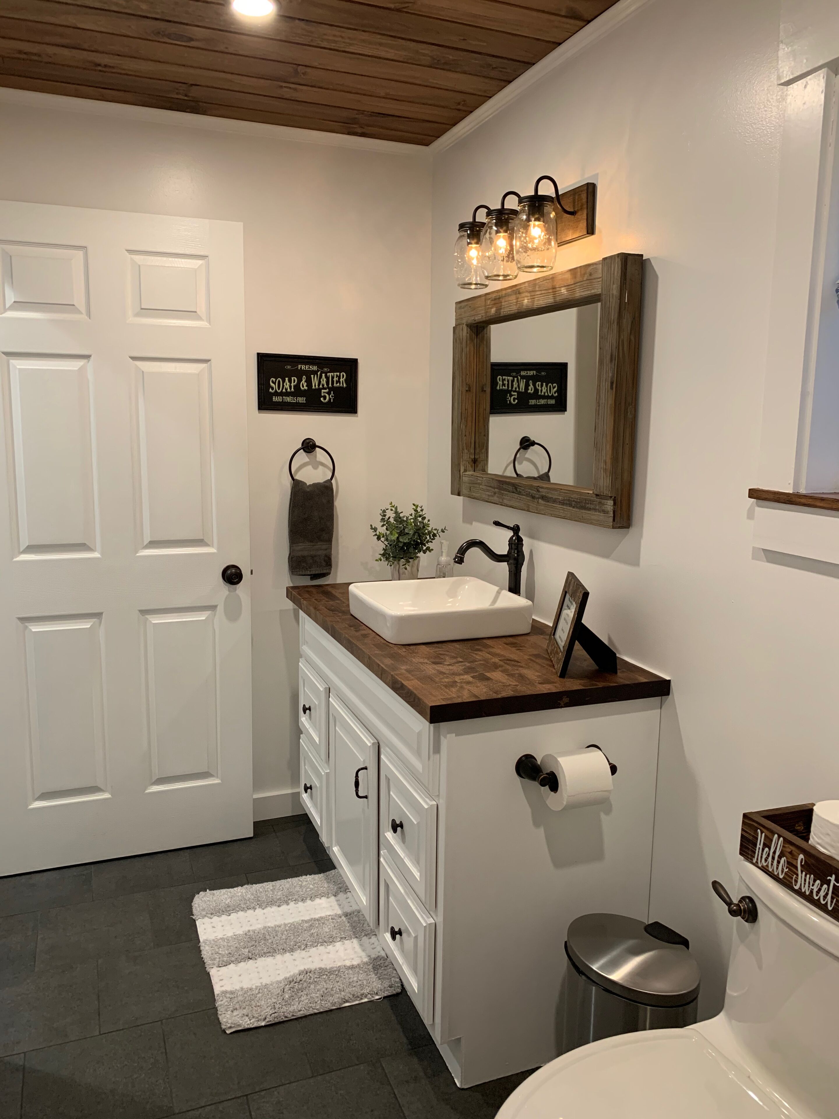 A bathroom with a white vanity, a mirror, a towel rack, a sink, a toilet, and a trash can.