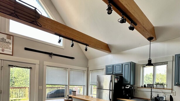 A modern kitchen with wooden beams, a long countertop, and three stools.