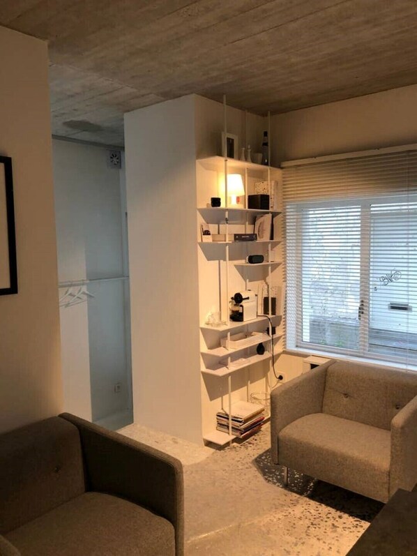 Relax in a bright, airy space with a shelving unit, comfortable armchairs, and large window.