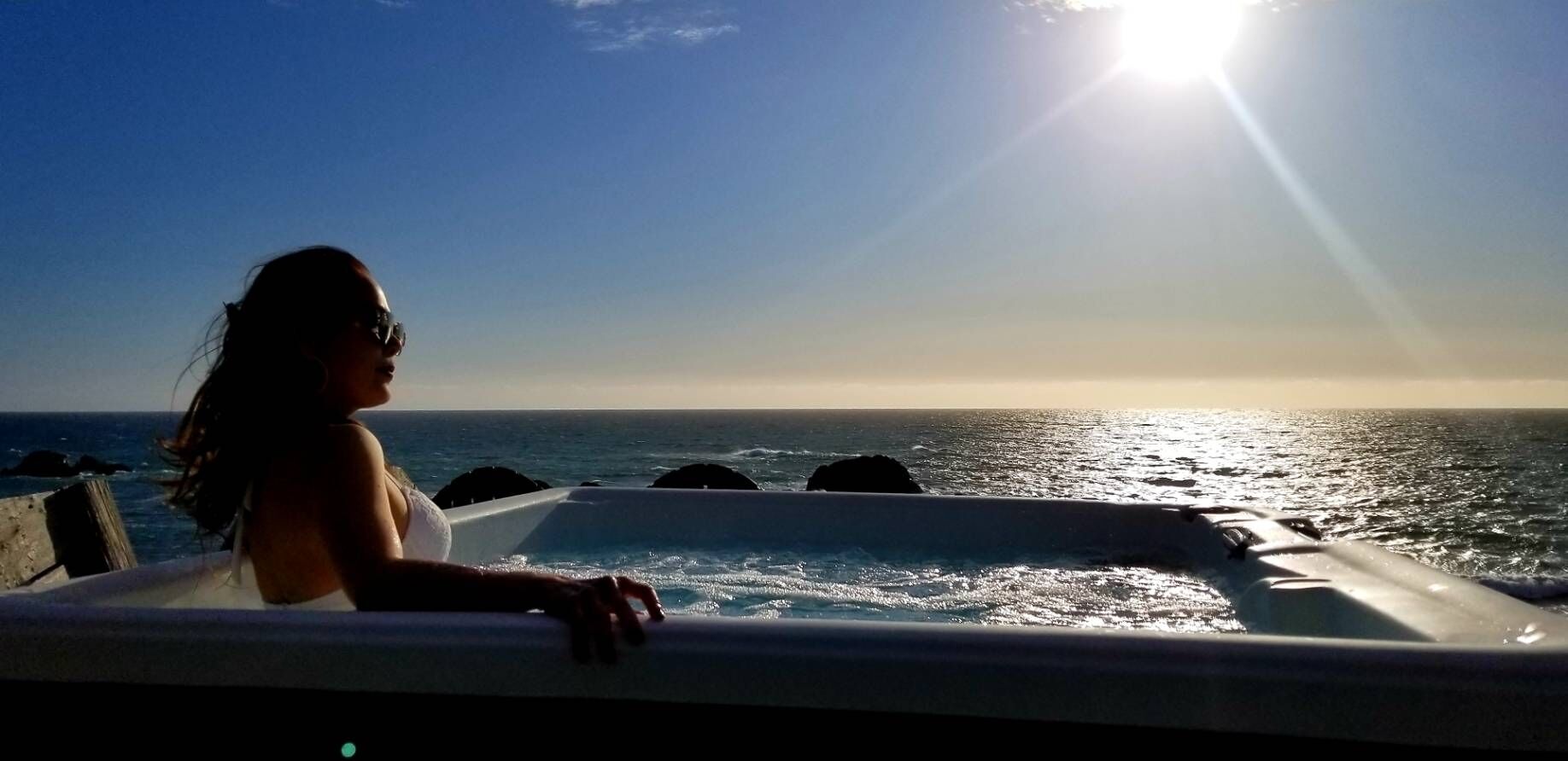 Una persona en una bañera con vistas al océano y al atardecer.