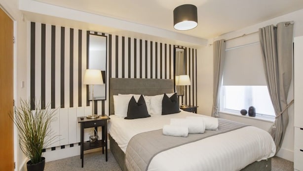 Een hotelkamer met een groot bed, nachtkastjes, een kamerplant, een raam met gordijnen en een gestreept wandontwerp.