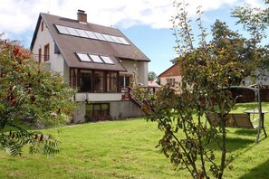 Una casa de dos pisos con techo inclinado, paneles solares, un pequeño porche delantero y un césped bien cuidado.