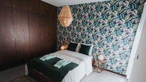 Ein Schlafzimmer mit Bett, dekorativer Tapete, einer Pendelleuchte und einem kleinen Nachttisch.