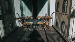 Ein Balkon mit Holztisch und -stühlen, einer Laterne und Blick auf ein Gebäude mit Rundbogenfenstern.