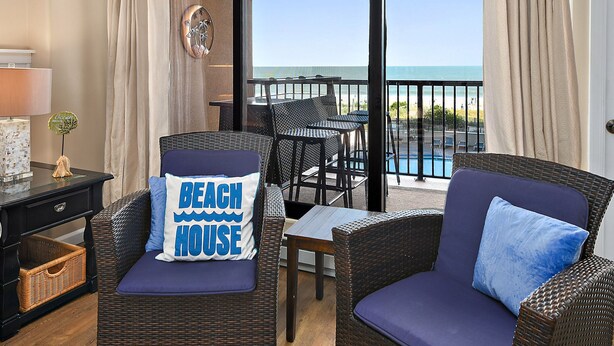 Un balcón con mobiliario de mimbre, vista al océano y un letrero que dice 'Beach House'.