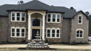 A two-story house with a stone facade, multiple windows, and a central entrance with a decorative fountain. - Newly Built House Close to Masters (Evans)