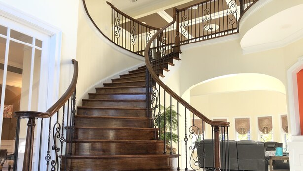 A grand spiral staircase with dark wood steps and ornate metal railings, leading to an upper floor. - Newly Built House Close to Masters (Evans)
