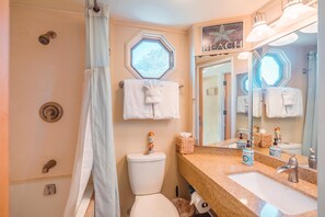 Une salle de bain avec des toilettes, un lavabo et une douche. Des serviettes sont accrochées au mur et il y a une fenêtre au-dessus des toilettes.