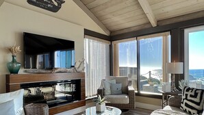 A modern living room with a fireplace, comfortable seating, and large windows offering a view of the ocean. - Seamist Beach Cottage (Bodega Bay)