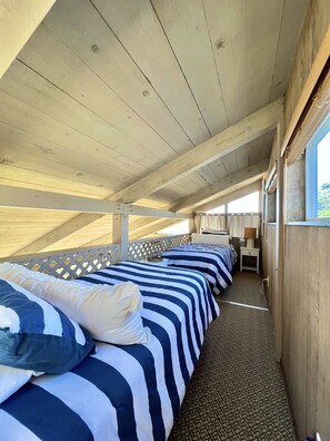 A row of beds with striped bedding, a wooden ceiling, and a window on the right.