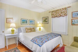 Quarto com cama, duas luminárias de apoio, uma janela com persianas e uma porta.