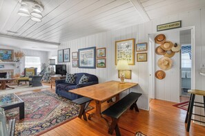 Uma sala de estar acolhedora, com uma mesa de madeira, sofá azul e várias fotos emolduradas nas paredes.