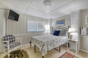 A bedroom with a bed, a chair, a bedside table with a lamp, a painting on the wall, and a television mounted on the wall. - Miller Villa, 6 bedroom, 3 bathrooms, deep water channel (Murrells Inlet)